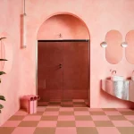 Sıvalı duvarları, karo zemini ve füme cam duş perdesi olan pembe banyo