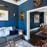 Mavi duvarlı ve ahşap zeminli küçük bir oturma odası, lacivert duvarlı bir yemek odasına açılıyor.