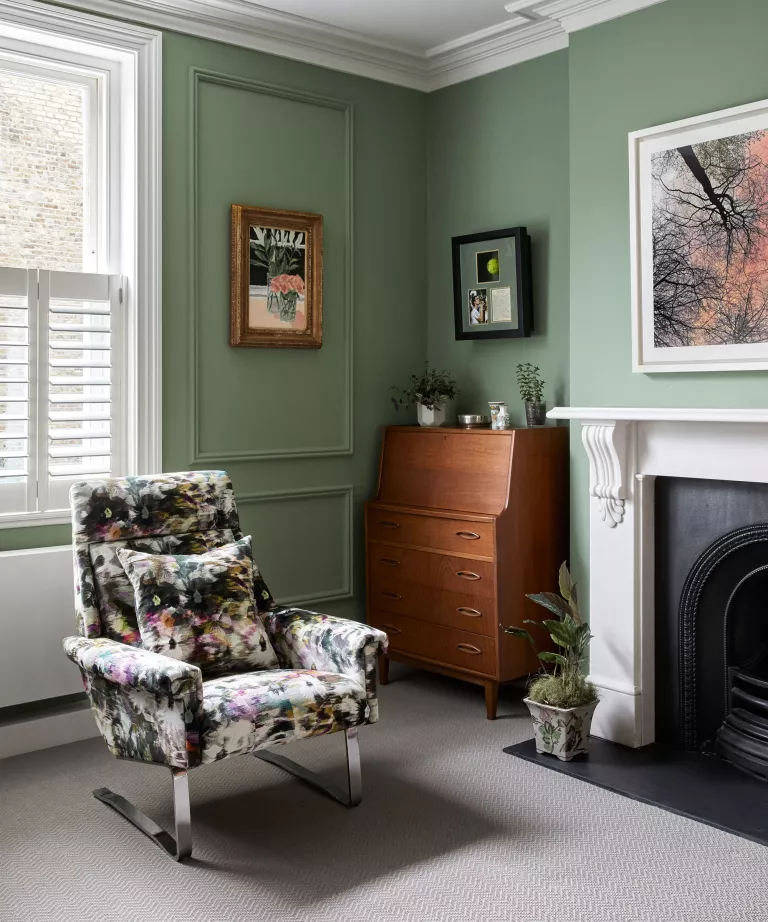 Yeşil panelli duvarları, gri halısı ve desenli koltuğu olan oturma odasının bir köşesi.